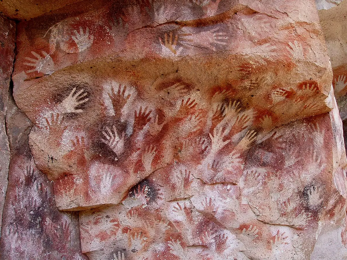Prehistoric outlines of dozens of hands in orange, brown, and black on a cave wall